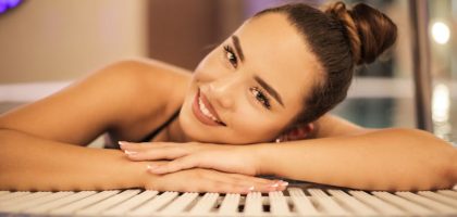 A happy woman with a bun relaxing and smiling at an indoor poolside, creating a warm and inviting atmosphere.