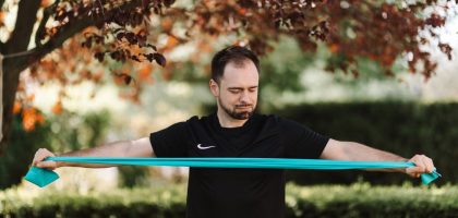 Man using resistance band for exercise in a sunny outdoor setting.