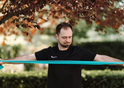 Man using resistance band for exercise in a sunny outdoor setting.