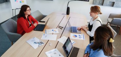 Three women in an office setting discussing business documents on laptops and paper.